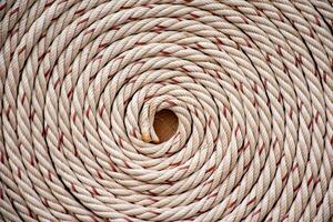 White rope with red lines and coiled roll from top view on wooden table background in warm tone. Braided rope on a roll background texture 2025. Photo of an old vintage rope.