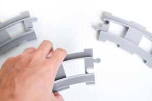 Hand holding gray toy railroad tracks put in on white background. Hand holding the railroad tracks to connect them together for the concept of connection and collaboration. photo