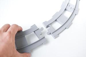 Hand holding gray toy railroad tracks on white background. Hand holding the railroad tracks to connect them together for the concept of connection and collaboration. photo