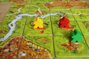 board family game carcassonne green yellow red meeple on the map tiles of the playing field. Rules for placing monasteries on carriages photo