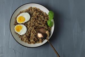 buckwheat porridge in a bowl chicken egg spoonful basil on a gray background with space for text copyspace photo