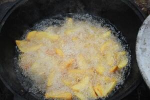 Potatoes are fried in a large pan in a cauldron, close-up view from above. Cooking in nature photo