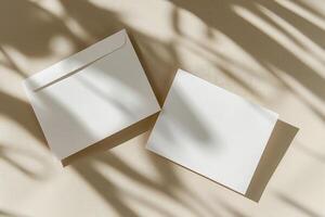 Flat lay of two rectangular blank cards and white envelope on ivory background with shadows. Top view photo