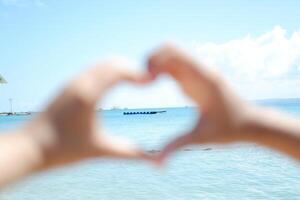 Hands forming a heart shape with the sea in the background. photo