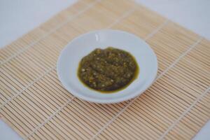 green sambal in a white bowl on a bamboo mat. photo
