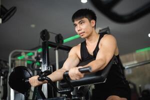 Asian man is working out in a gym, lifting weights and doing pushups. The gym is filled with various exercise equipment, including a bench and a machine. The atmosphere is energetic and focused photo