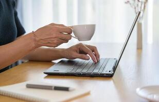 Freelance woman working from home office. Female using notebook computer while sipping coffee photo