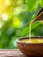 golden liquid pouring from green leaf into clay bowl with blurred green background. photo