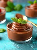 delicious chocolate mousse with mint garnish in glass cup on turquoise background. photo