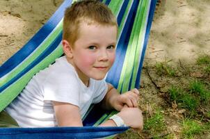 Cute little blond caucasian boy relaxing and having fun in multicolored hammock photo