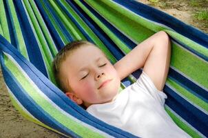Cute little blond caucasian boy relaxing and having fun in multicolored hammock photo