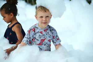 happy little boy with foam on his head, in wet clothes at a foam party photo