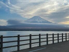 Mount Fuji view from across a lake, with a wooden railing in the foreground. photo