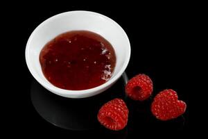 raspberries and jam on black. Jar with delicious raspberry jam. Raspberries and Jelly photo