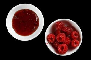 raspberries and jam on black. Jar with delicious raspberry jam photo