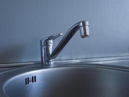 Metal faucet and metallic washbasin captured in detail. Close-up of metal faucet with water flow. Focus on modern design and functionality of metal faucet in sleek metallic washbasin. photo