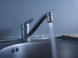 Close-up of faucet and a jet of water pouring into the sink. Observe the steady flow from the faucet, showcasing the clarity and force of water. The faucet provides a consistent and powerful stream. photo