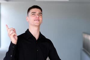 The young man in the shirt shows his finger on the empty space for copying the text while standing in modern office. Smiling handsome mixed race businessman looking at camera. Template for advertising photo