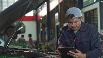 Asain Young man mechanic working in repair shop Use a tablet while repairing an engine in a car service center. video