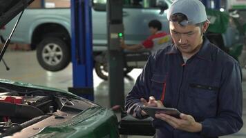 Asain Young man mechanic working in repair shop Use a tablet while repairing an engine in a car service center. video