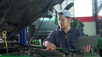 Experienced indian mechanic in uniform is using a laptop while repairing car in auto service video