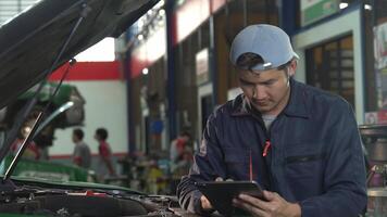 Asian auto mechanic using a tab car inspection and measure the oil level on the vehicle's engine dipstick. car oil quality. video
