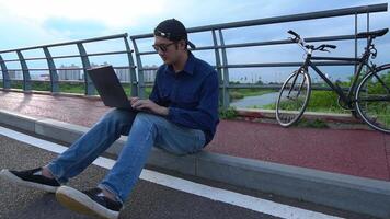 Asian man sitting on the curb with an open laptop in front of him The scene is calm and relaxing. The man was enjoying his time working or surfing the internet. video