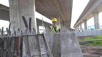 A construction supervisor Use a laptop to monitor this concrete casting taking place on a construction site under a highway bridge. video