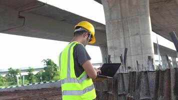 A construction supervisor Use a laptop to monitor this concrete casting taking place on a construction site under a highway bridge. video