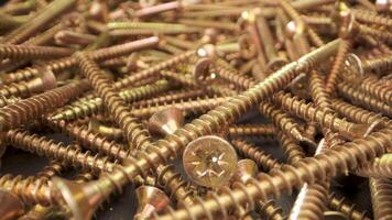 Close up view of a pile of gold screws. The screws are arranged in a random pattern and are illuminated by a bright light. The captures details of the screws, including the threads and the heads video