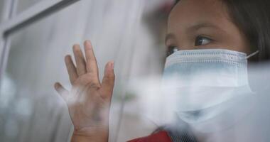 Asian girl wearing a surgical mask is looking out of the window and touching window. video