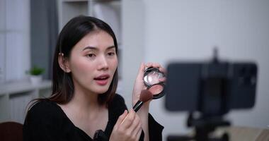 Handheld shot, Beautiful asian woman blogger is showing how to makeup and use cosmetics. In front of the smartphone to record vlog video live streaming at home. Influencer and cosmetics concepts.