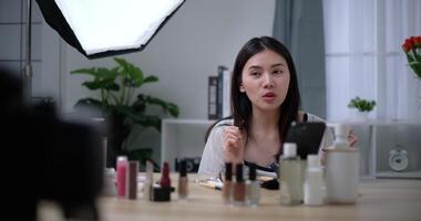 Footage of Beautiful asian woman blogger is showing how to makeup and use cosmetics. In front of the camera to record vlog video live streaming at home. Influencer and cosmetics concepts.