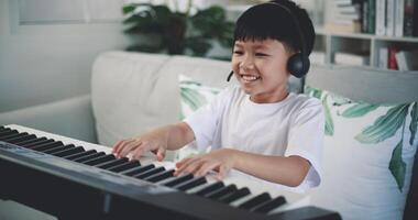 Handheld shot, Creative asian boy wearing headphone with artistic skills taking music lessons online during a video call and playing the piano at home. Music, hobby and lifestyle concepts.