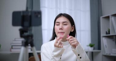 Handheld shot, Beautiful asian woman blogger is showing how to makeup and use cosmetics. In front of the smartphone to record vlog video live streaming at home. Influencer and cosmetics concepts.