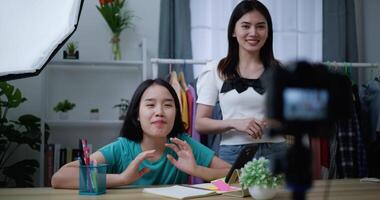 Footage of Young Beautiful Asian women live streaming at clothes shop, They are talking in front of camera and check comment on smartphone, small business online influencer on social media concept video