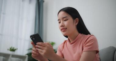 Footage of Happy young asian woman relax on comfortable couch at home shopping online on smartphone, smiling girl use cell phone chatting, browse wireless internet on gadget video