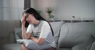 Footage dolly shot, Unwell young woman massaging temples to relieve headache with eyes closed while sitting on sofa at home, healthcare woes video