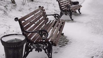 Snow is falling on empty city park. A lonely snow-covered bench stands near sea. Christmas Winter New Year Scenery background. Frosty winter in the city after snowfall video