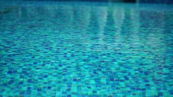 Pool water background with wavy clear fresh water. Calm rest on sunny day. Abstract reflections on the surface of the water with texture of bright blue pool tiles. Turquoise water surface. Slow motion video