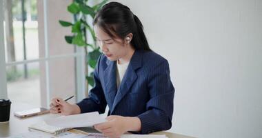 Footage high angle view shot, Asian businesswoman in suit sits on table while analyze documents and taking notes in small coffee shop. Work from anywhere, Remote working video