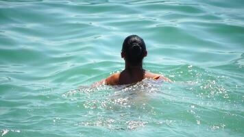 Woman swimming in calm sea at sunset, slow-motion, back view. Concept of body image and fitness, enjoying a serene beach. Happy woman with perfect fit body enjoys sea beach video