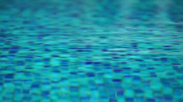 Pool water background with wavy clear fresh water. Calm rest on sunny day. Abstract reflections on the surface of the water with texture of bright blue pool tiles. Turquoise water surface. Slow motion video