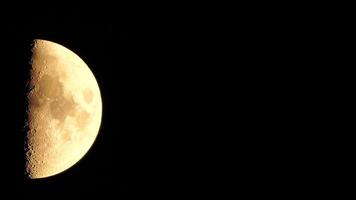 A glowing golden huge half moon seen from earth through the atmosphere against a starry night sky. A large moon moves across the sky, the moon moving from the left frame to the right. video