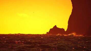 Red burning sunset, with a cliff in the background. The golden warm waters and its small wave ripples, along with bokeh lights from the sun. Abstract nature summer ocean sea. video