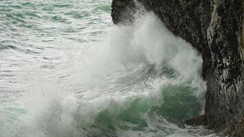 Stormy sea on sunset. The waves crash into the volcanic basalt rock, lit by the warm sunlight. Big wave breaks into splashes and white foam. Never-ending beauty of nature. Slow motion. video