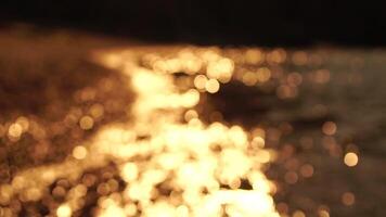 Abstract sea summer ocean sunset nature bokeh background. Small waves on azure water surface in motion blur with golden bokeh lights from sun. Holiday, vacation and recreational concept. Slow motion video