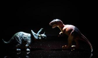 two dinosaurs, a tyrannosaurus rex and a triceratops fight in a realistic prehistoric setting illuminated by the moon photo