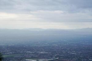 Top view of mountain in Chiang Mai City, Thailand. White cloud and dust is above of the mountain while cities can be seen far away. photo