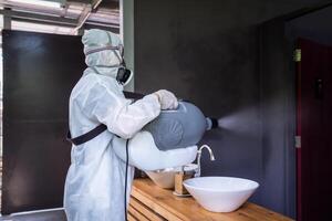 Professional technical man in prevention suit with his sterilizing machine and disinfecting water sprays in toilet or wc area field for purifying coronavirus COVID-19 photo